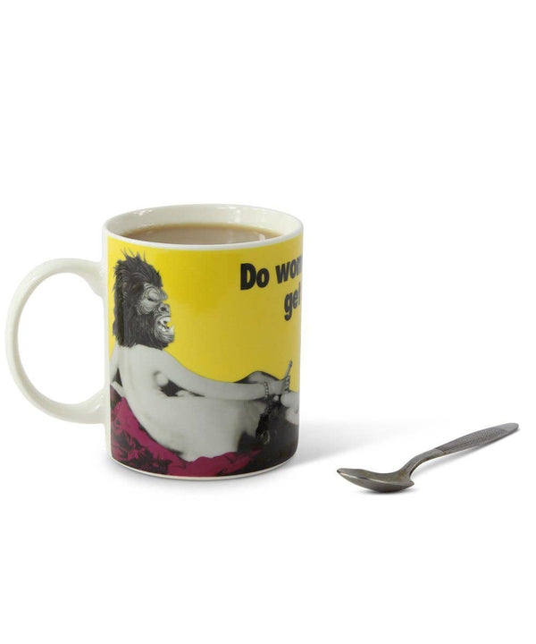 A yellow mug on a white surface. It has a naked woman in a gorilla mask printed on them, as well as the text "Do Women Have To Be Naked to get into the Met Museum?"