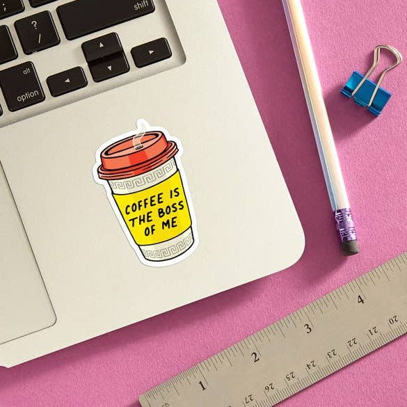 A sticker of a colorful coffee to go cup with a red lid attached to a laptop. The text reads "Coffee is the Boss of Me."