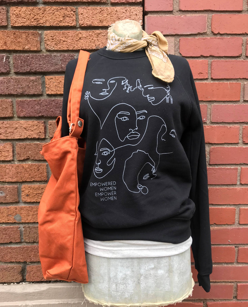 Mannequin wearing a black crewneck with white line illustrations of women's faces.