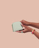 A hand is holding up a light blue vegan leather wallet.