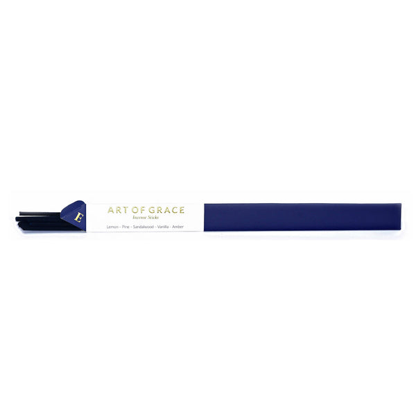 A white background with incense in the forefront of the image. The package is navy blue with a strip of white making up a third of the packaging. In golden lettering are the words "Art of Grace." In smaller text are the words "Lemon, Pine, Sandalwood, Vanilla, Amber" these words are being used to describe the fragrance of the incense