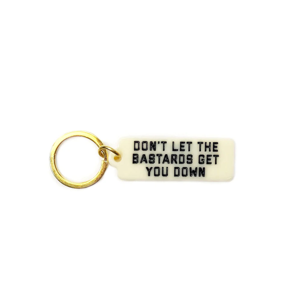 A golden keychain with a white key tag. The text reads "Don't Let the Bastards Get You Down."