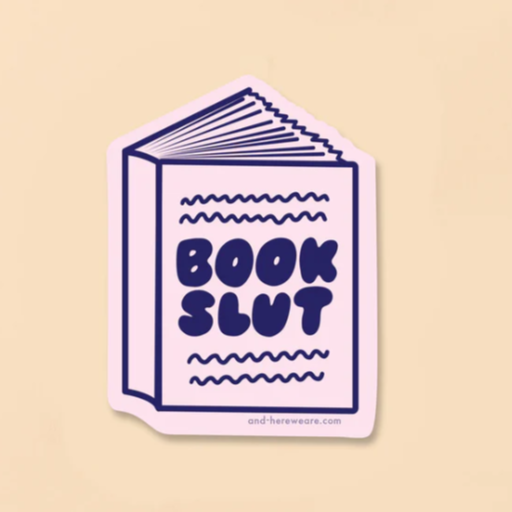 A beige background with a pink sticker in front of it. The sticker is in the shape of a book with the words "Book Slut" in navy letters. 