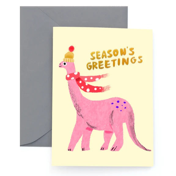 A yellow greeting card with an illustration of a pink dinosaur wearing a wool hat and a red scarf. The text reads "Season's greetings."