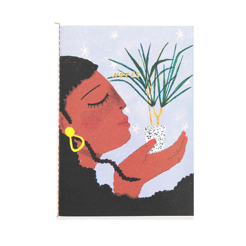 A notebook with an illustration of a woman with a dark skin tone and long black hair in profile holding up a flower.