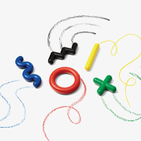 A white background with various crayons before it. The crayons are in the shape of a red circle, a blue squiggle, a yellow line, a green "X", and a black zig-zag. Each crayon has marked the surface of the white background with its respective color. 
