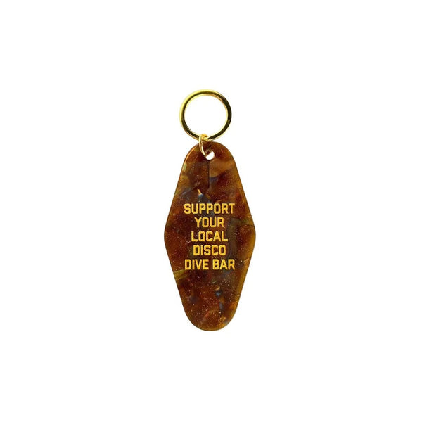 A white background with a tortoise shell keytag before it. The keytag reads "Support Your Local Disco Dive Bar."