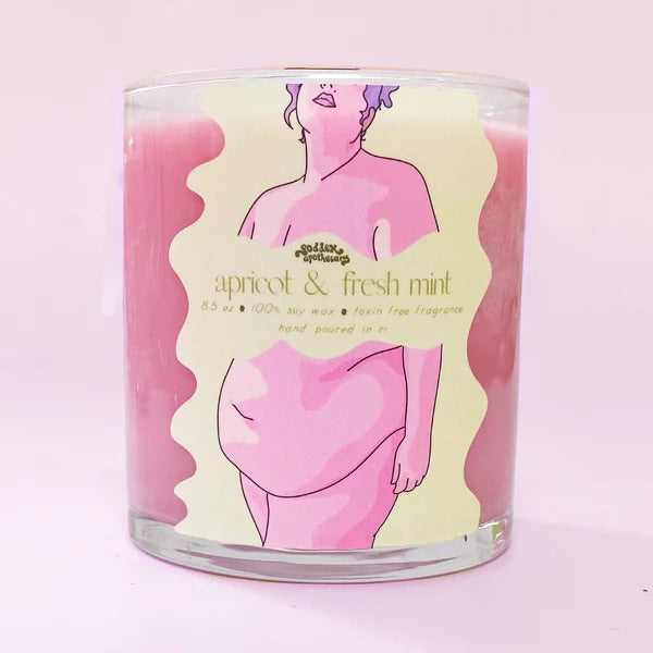 A pink candle in a glass. A sticker on the glass shows a woman's body and the text: "Apricot and fresh mint."