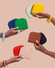 Several hands are holding colorful vegan leather wallets.