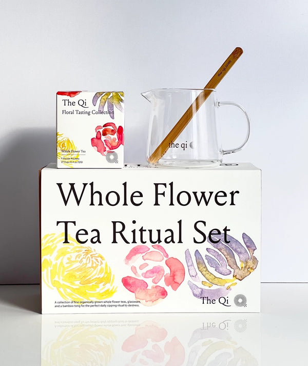 A white box with a box of tea and a glass tea mug standing on top of it. The box has watercolors of flowers and text reading "Whole Flower: Tea Ritual Set."