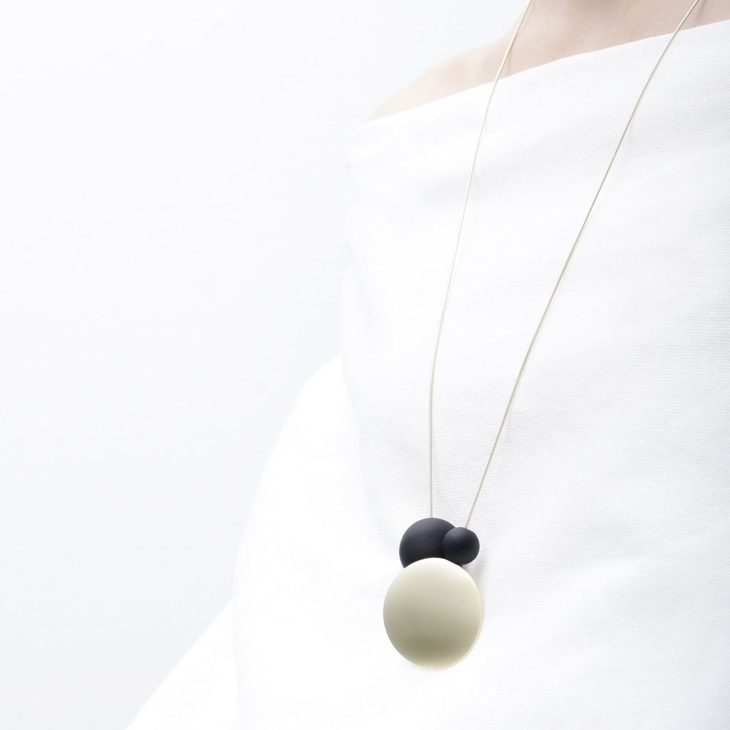 Long necklace with a statement pendant in the shape of three orbs in black and gold.