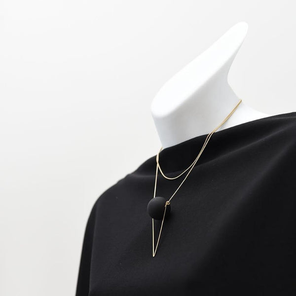 A long silver necklace with a black orb hanging on a mannequin wearing a black shirt.