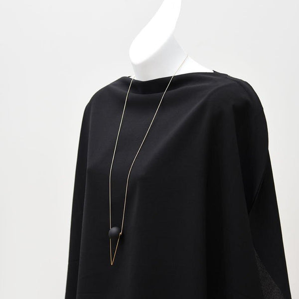 A long brass necklace with a black orb hanging on a mannequin wearing a black shirt.