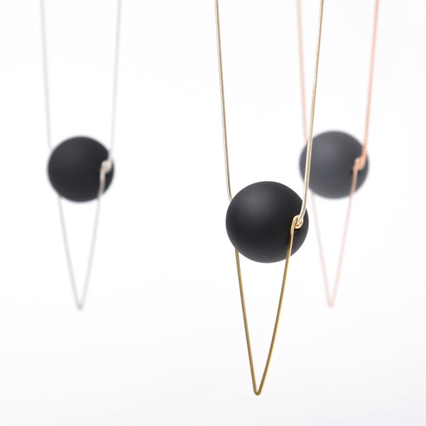 A brass chain with a black orb hanging on it. Two other necklaces with silver and rose-gold chains are hanging behind it.