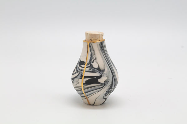 A small marble vase with golden details and a cork lid.