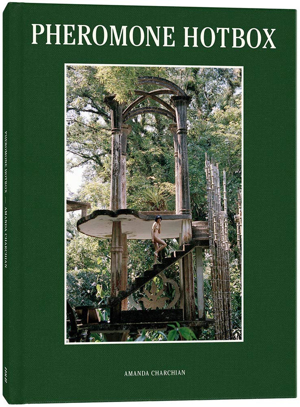 A book cover in green with a large photograph of an architectural structure in a forest and a naked woman walking up the stairs. The title reads: Pheromone Hotbox."