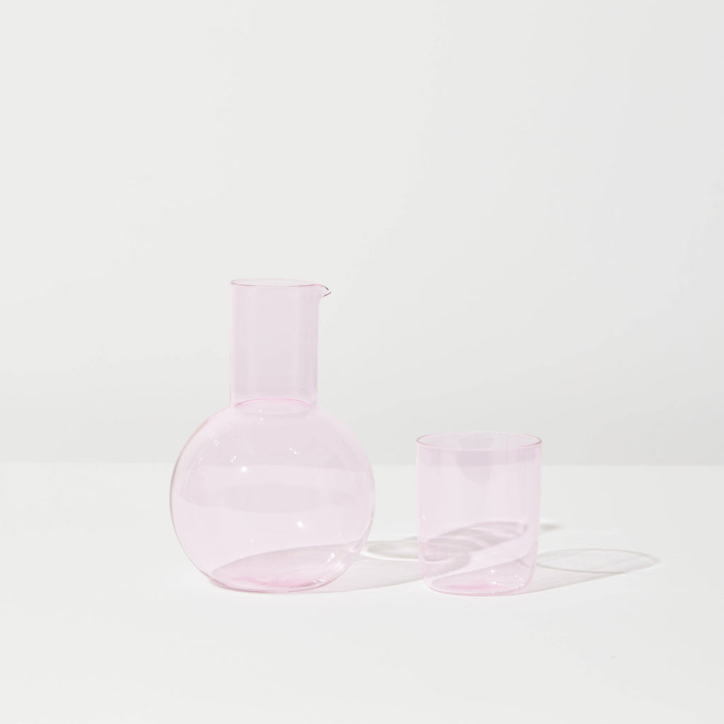 A pink carafe with a round body and a small neck and a mug standing next to it. 
