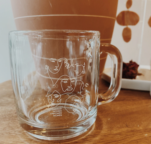 Empty glass mug with line drawings of women's faces and the text "Empowered women empower women."