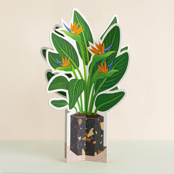 A 3-D paper plant with colorful flowers in a black pot with a speckled pattern. 