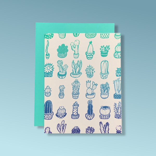 A greeting card with an illustration of several rows of cacti next to each other, drawn in blue. The card is in a light peach tone and comes with a blue envelope.