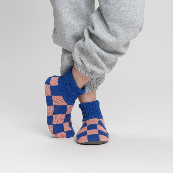 A person is modeling knit fleece-lined slippers with a checkerboard pattern in pink and blue.