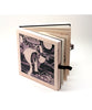Small artist book with a black and white cover featuring an illustration. Small leather straps are holding the book together.