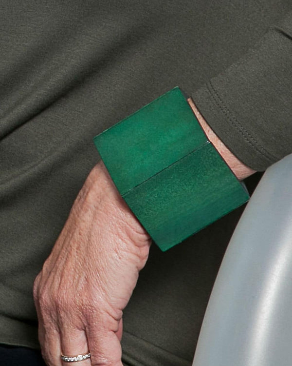 A person wearing a chunky wooden geometric bracelet in a dark forest green before a white background. 
