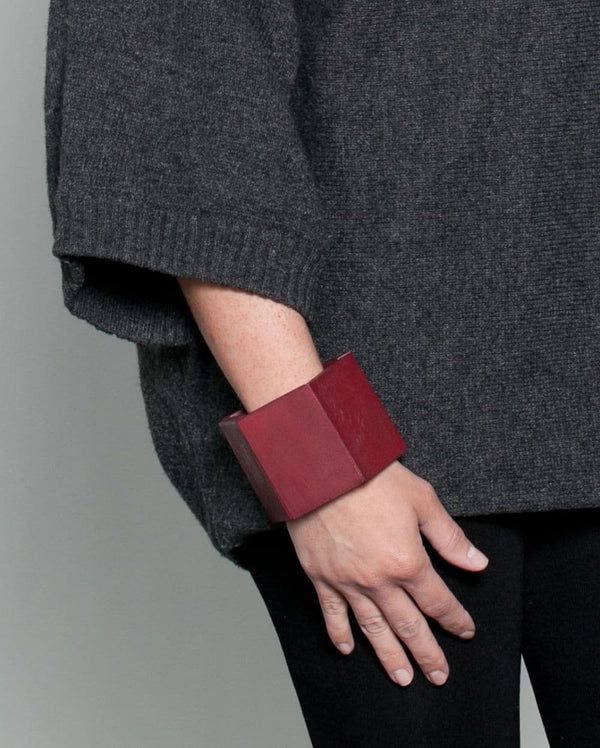 A person wearing a chunky wooden geometric bracelet in a red before a white background. 