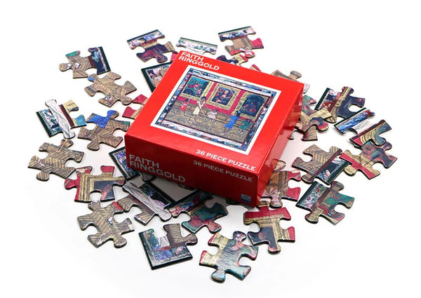 A puzzle laid out on a table and a red box that reads "Dancing at the Louvre Puzzle x Faith Ringgold."