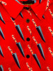 A close up of a garment. A red shirt with  a blue knive pattern printed on it. The shirt has black buttons.
