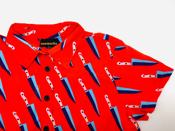 A red shirt with  a blue knive pattern printed on it. The shirt has black buttons.