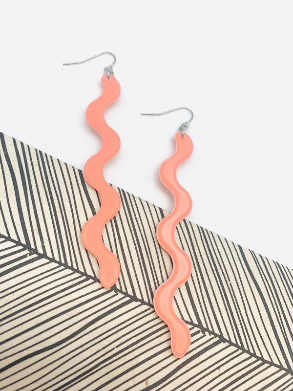 A pair of squiggle earrings in peach on a white and black background.