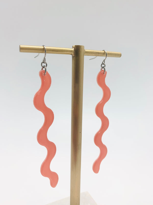A pair of squiggle earrings in peach on a golden stand.