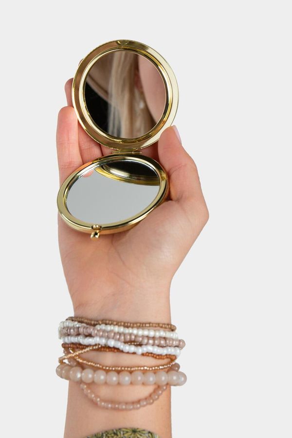 A hand holding a golden compact mirror. 