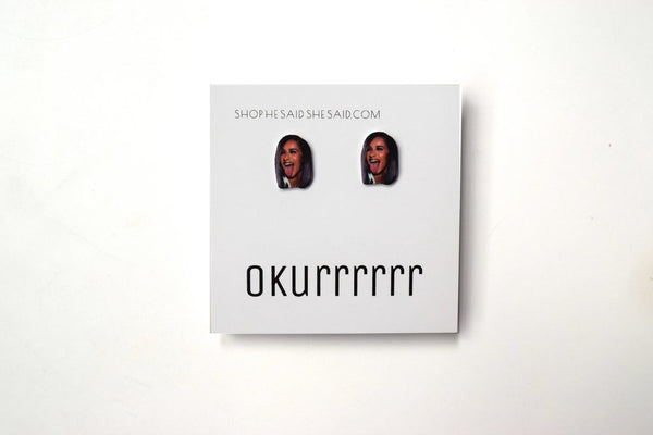 Two plastic earrings with a photograph of a woman showing her tongue. The woman has a dark skin tone. The earrings are attached to a paper card which reads "Okurrrrrrr."