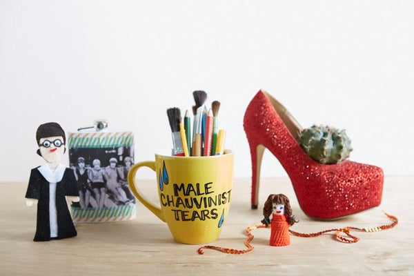 A yellow mug reading "Male chauvinist tears" next to hand puppets and a red high heel.
