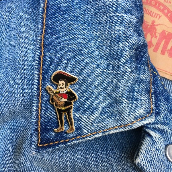 A denim background with a pin of a mariachi player before it. 