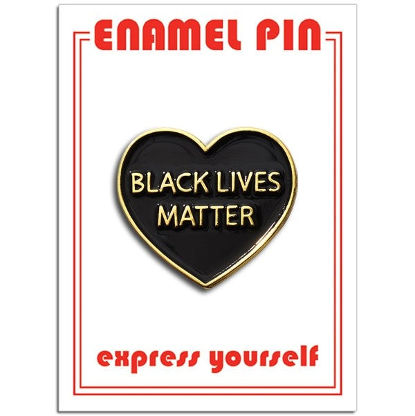 A black enamel pin in the shape of a heart with golden lettering. The text reads "Black Lives Matter" in all caps.