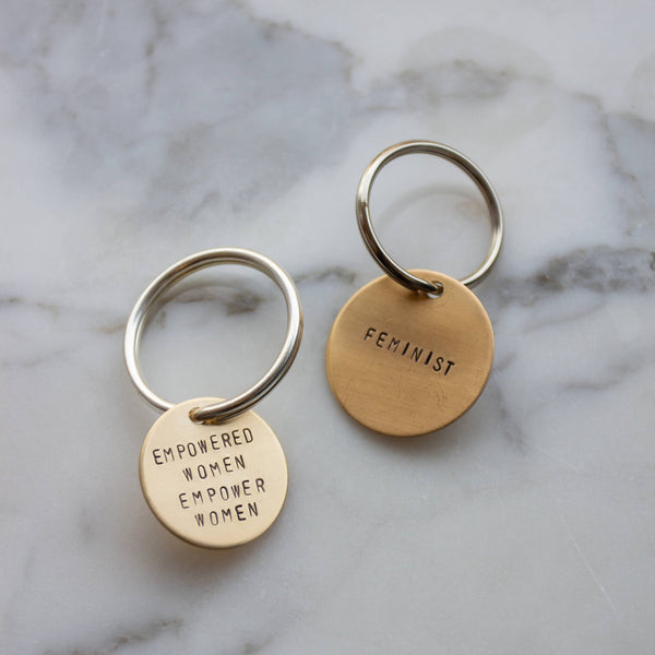 Two brass key rings with text written in capital letters. On one pendant, it reads "Empowered Women Empower Women", the other one reads "Feminist."