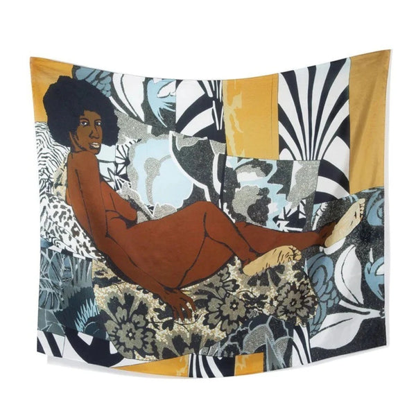 A white background with a scarf before it. The scarf depicts a famous artwork by Mickalene Thomas. This artwork features a nude, black woman with natural hair laying down and staring straight toward the "audience." She is laying on a variety of patterns and colors with an indistinct shape. 