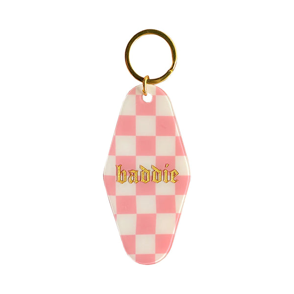 A white background with a keytag before it. The keytag features a pattern of pink and white checkers and the word "Baddie" written in gold lettering. 