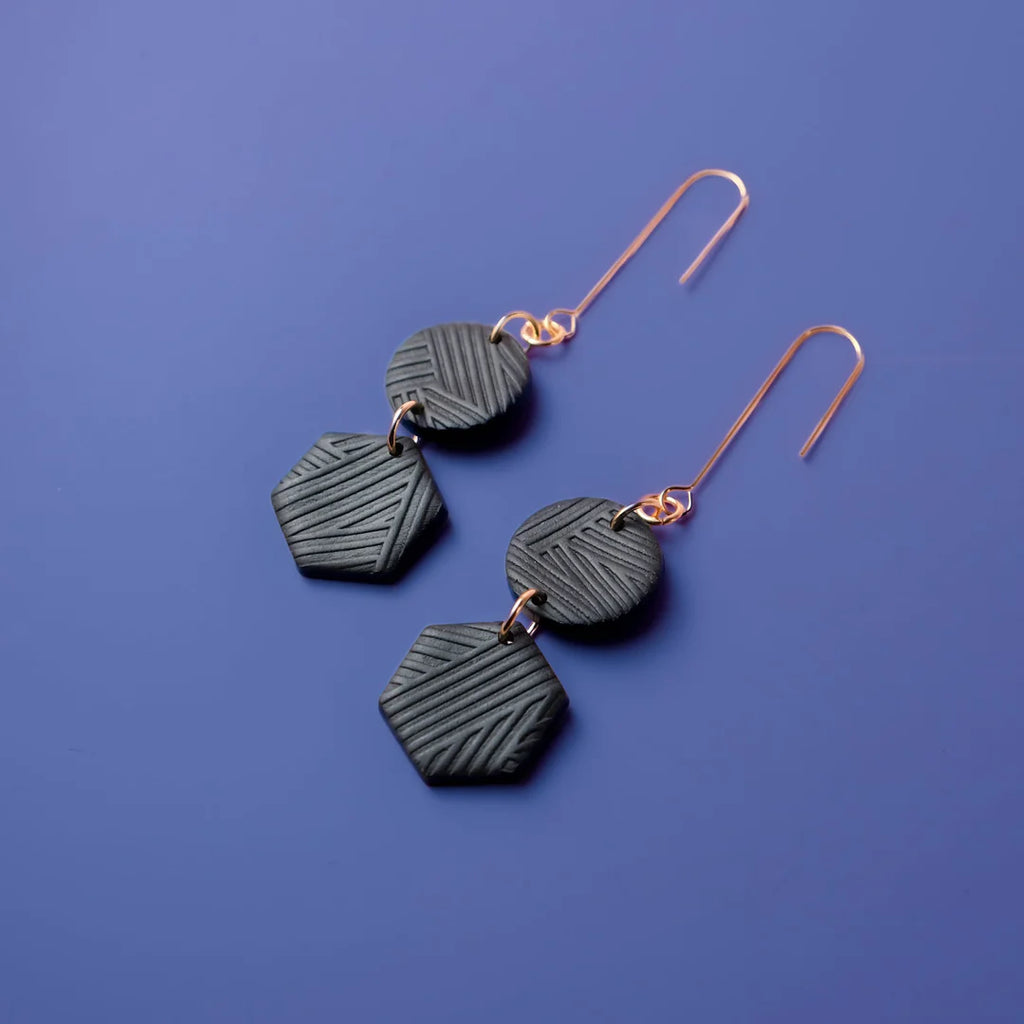 A set of two black, geometric earrings. They are attached to a rose-gold hook.