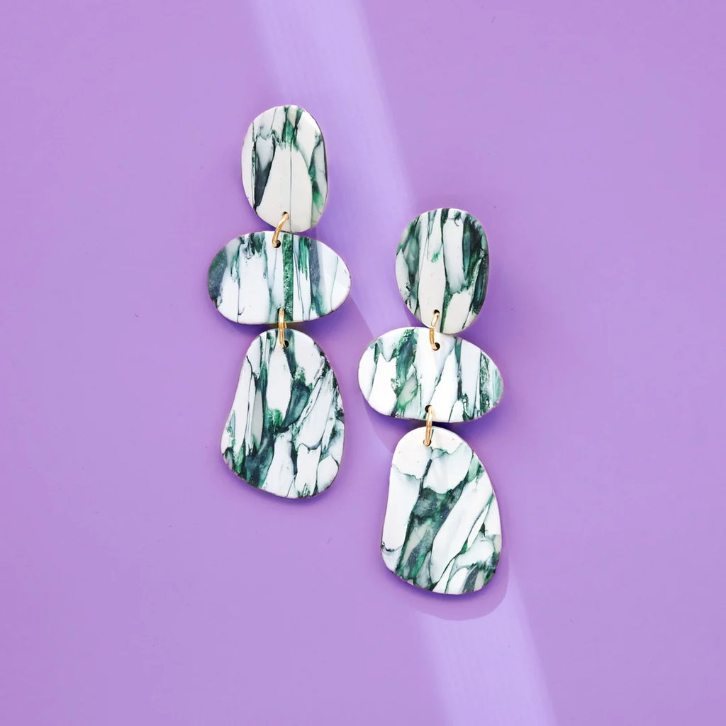 White and green clay earrings composed of organic shapes that resemble balancing rocks.