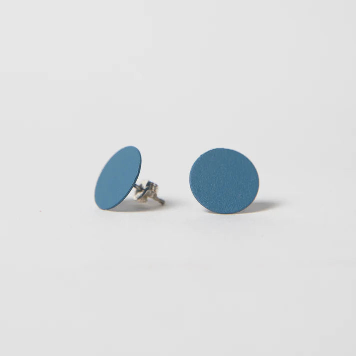 A white background with two earrings before it. The earrings are cobalt-colored studs that are in the shape of a circle.