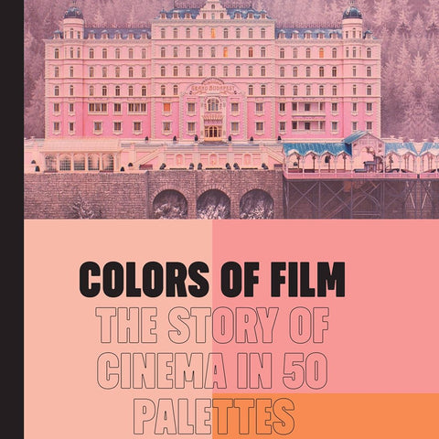 A pink book with a black binding. The book cover has an image of a still from the film "The Grand Budapest Hotel" which features a large pink hotel surrounded by mountainous forest. Below the image are three shades of pink and coral colors making up a geometric palette. The title of the book "Colors of Film: the Story of Cinema in Fifty Palettes" is written in black font.