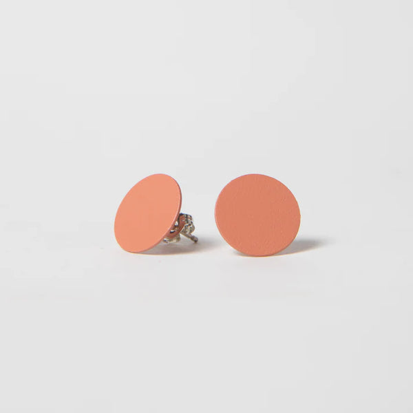 A white background with two earrings before it. The earrings are coral-colored studs that are in the shape of a circle.