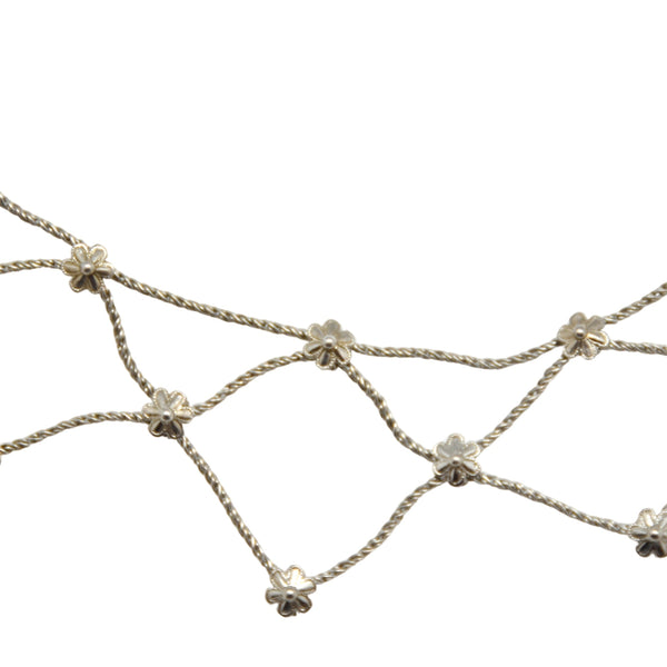 A white background with a silver necklace before it. The necklace is made up of a lattice of silver chains with floral accents.