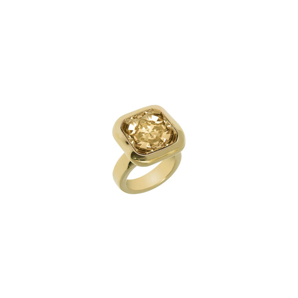 A white background with a golden ring in front of it. The ring has a square shaped setting and features a gold crystal. 
