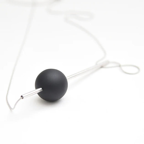 A white background with a necklace in front of it. The necklace has a black circular bead on it. There is a silver bar running through it. There is also a thin silver chain holding it together. 