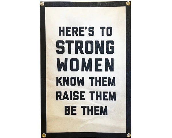 A white background with a black and white banner before it. The banner is white with a black border. The banner reads "Here's To Strong Women Know Them Raise Them Be Them" in black letters. 